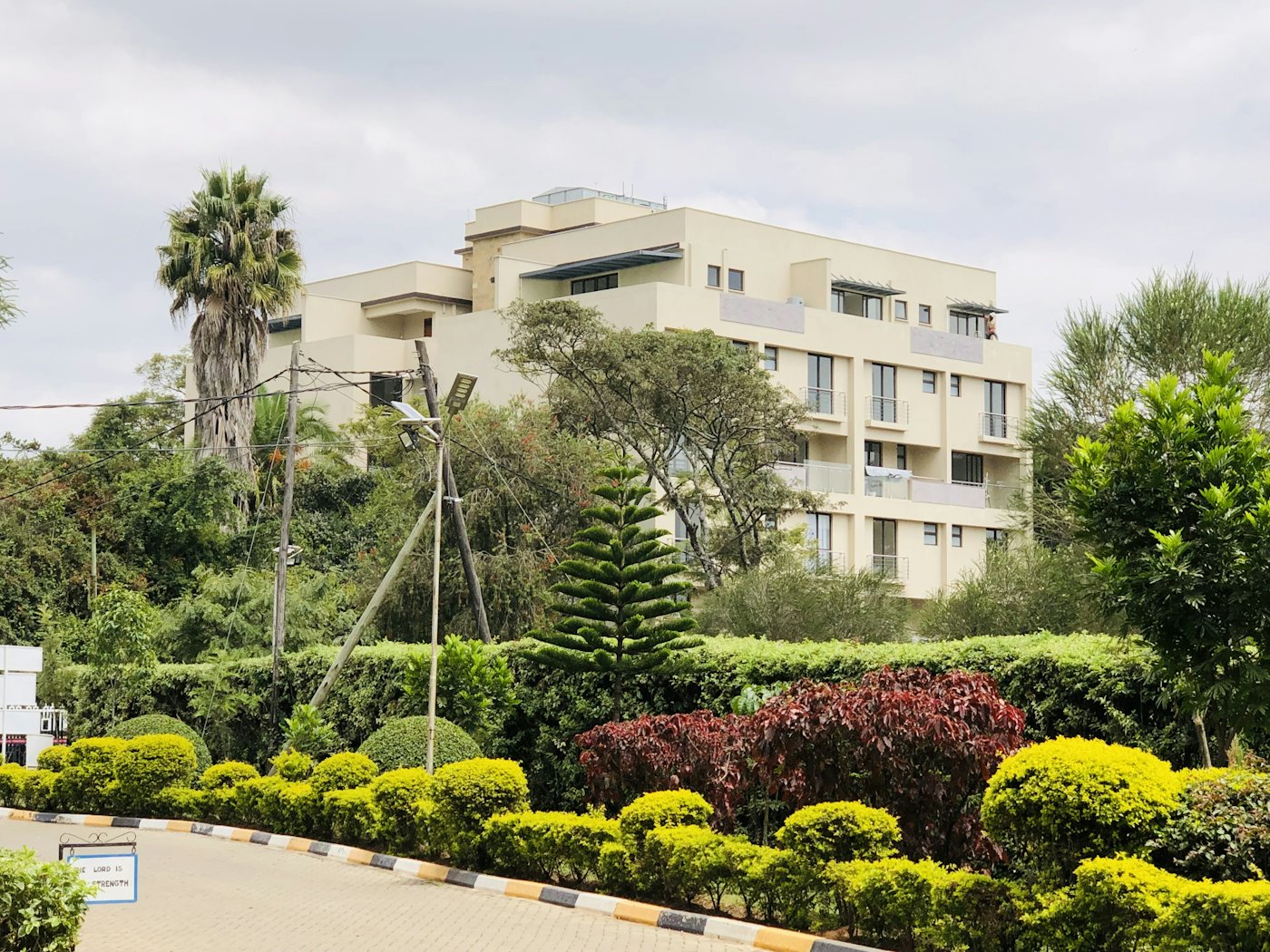 Cream apartment building with balconies above a landscaped driveway
